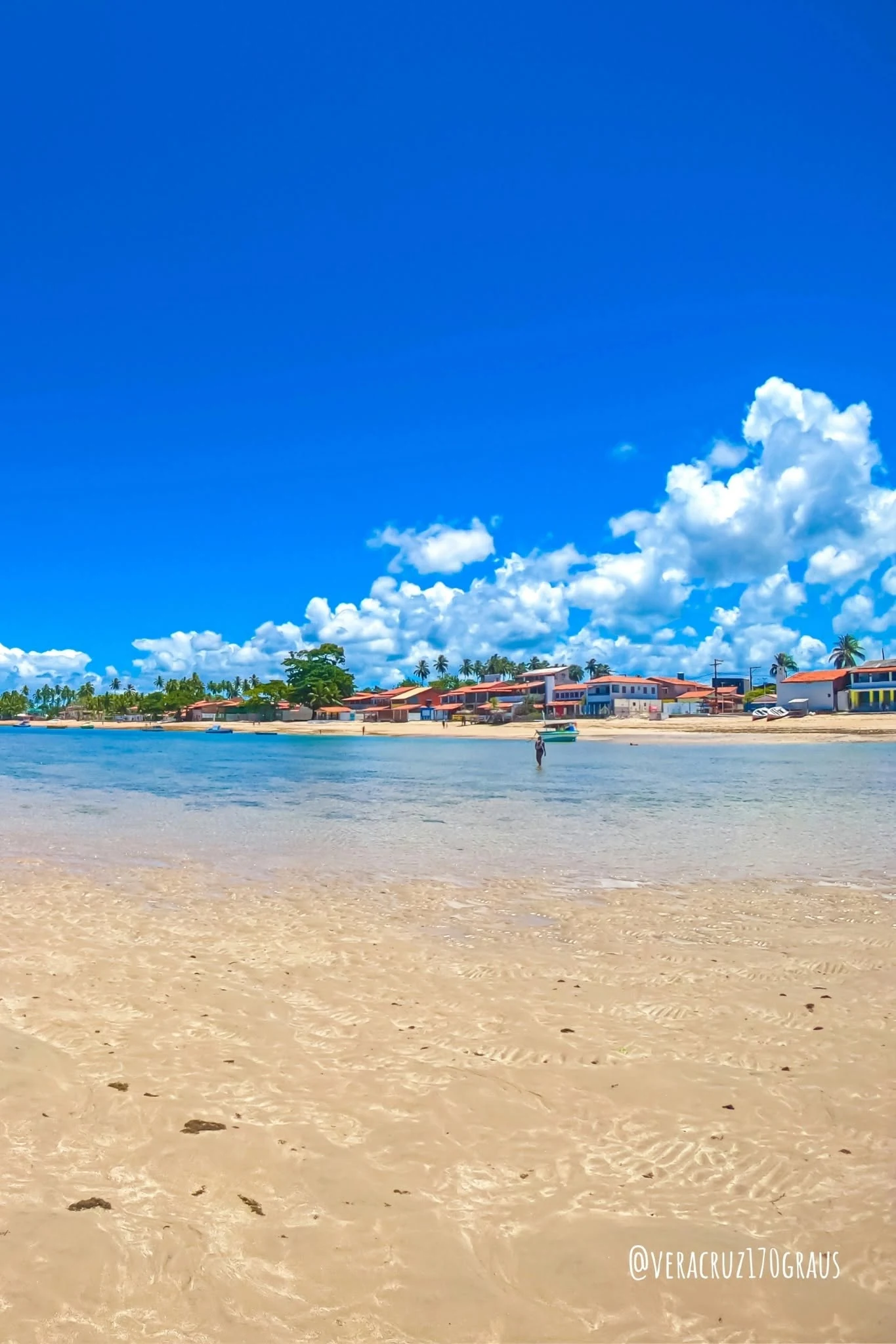 Praia de Catu com águas rasas e comunidade ao fundo