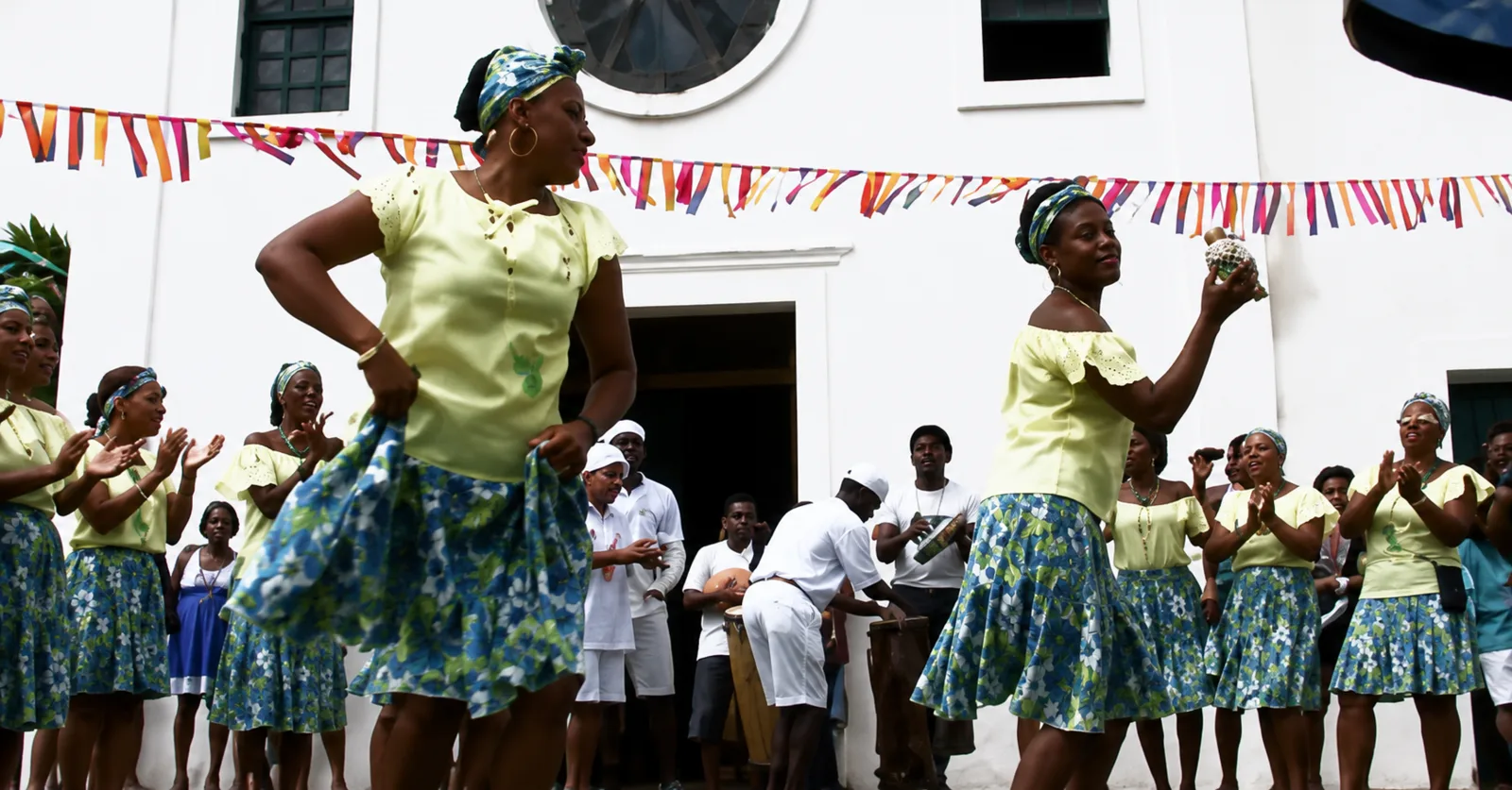 Grupo de mulheres dançando diante de uma igreja durante manifestação cultural
